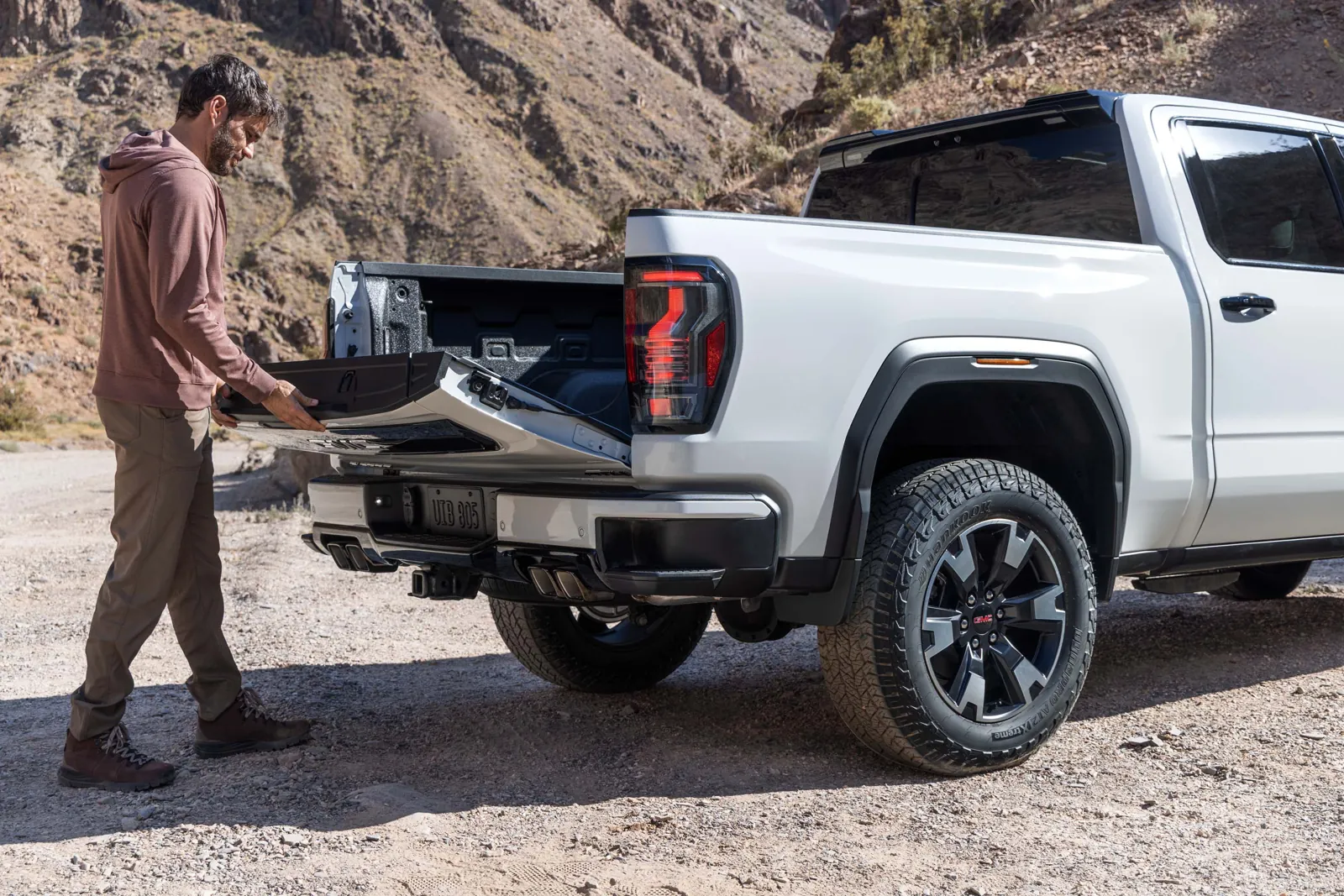 Man opening the MultiPro tailgate on a white 2027 GMC Sierra 1500